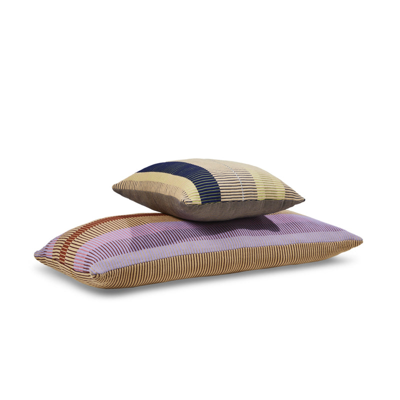 Two Ames Chumbes Cushions by Ames, hand-woven with textured fabric and horizontal stripes in beige, brown, purple, red, blue, and yellow, are stacked together.