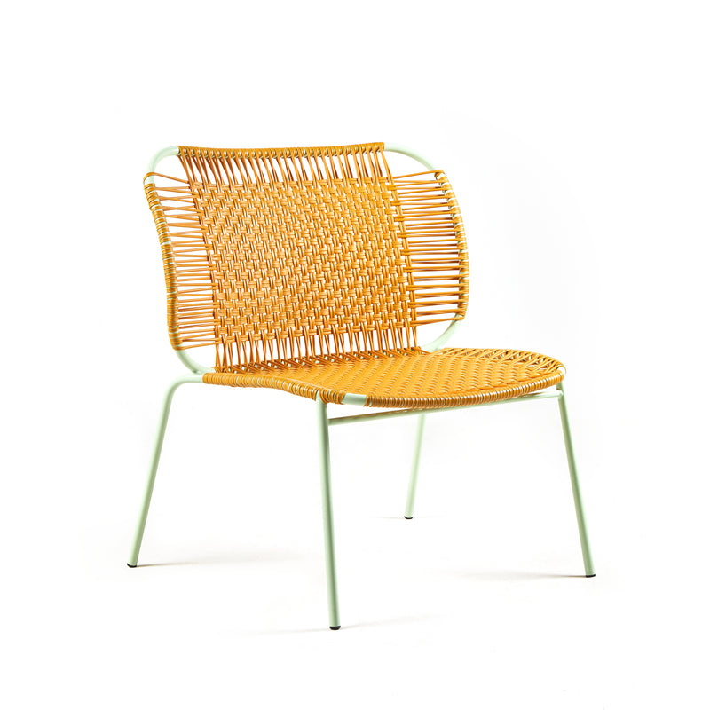 The Ames Cielo Lounge Chair Low by Ames features a stackable design with a woven yellow seat and backrest, slim light green metal legs, and is photographed against a plain white background. Suitable for both indoor and outdoor use.
