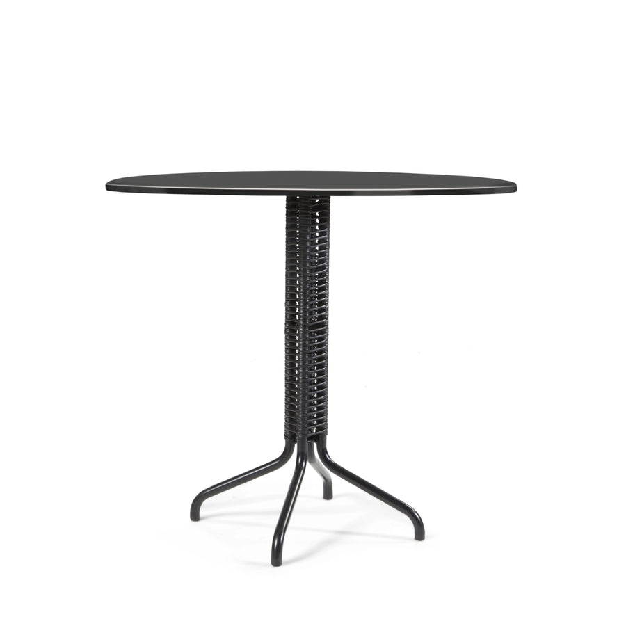 The Cielo Bistro Table by Ames, crafted with Sebastian Herkners signature style, features a compact design. It has a black round tabletop with a glossy finish on a wicker-style cylindrical base and three elegantly curved metal legs against a crisp white backdrop.