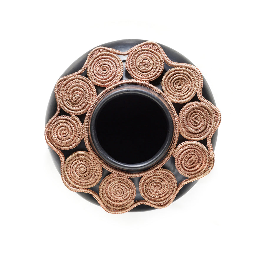 The Ames Coyar Vase 1 by Ames is a black ceramic vase seen from above, showcasing an intricate circular border of coiled wickerwork decoration around its opening.