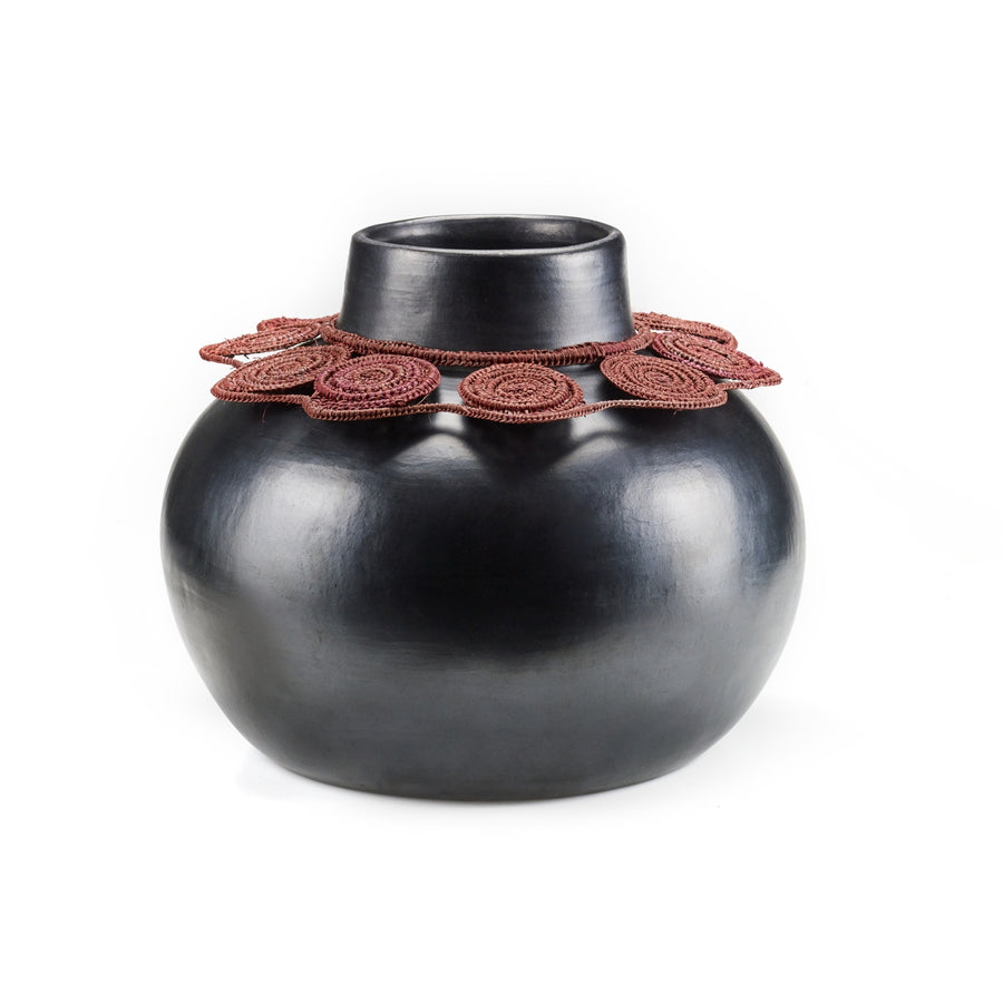 The Ames Coyar Vase 1 by Ames is a glossy, round black ceramic pot with a narrow neck, featuring an intricate red-brown wickerwork-inspired decorative band at the rim.