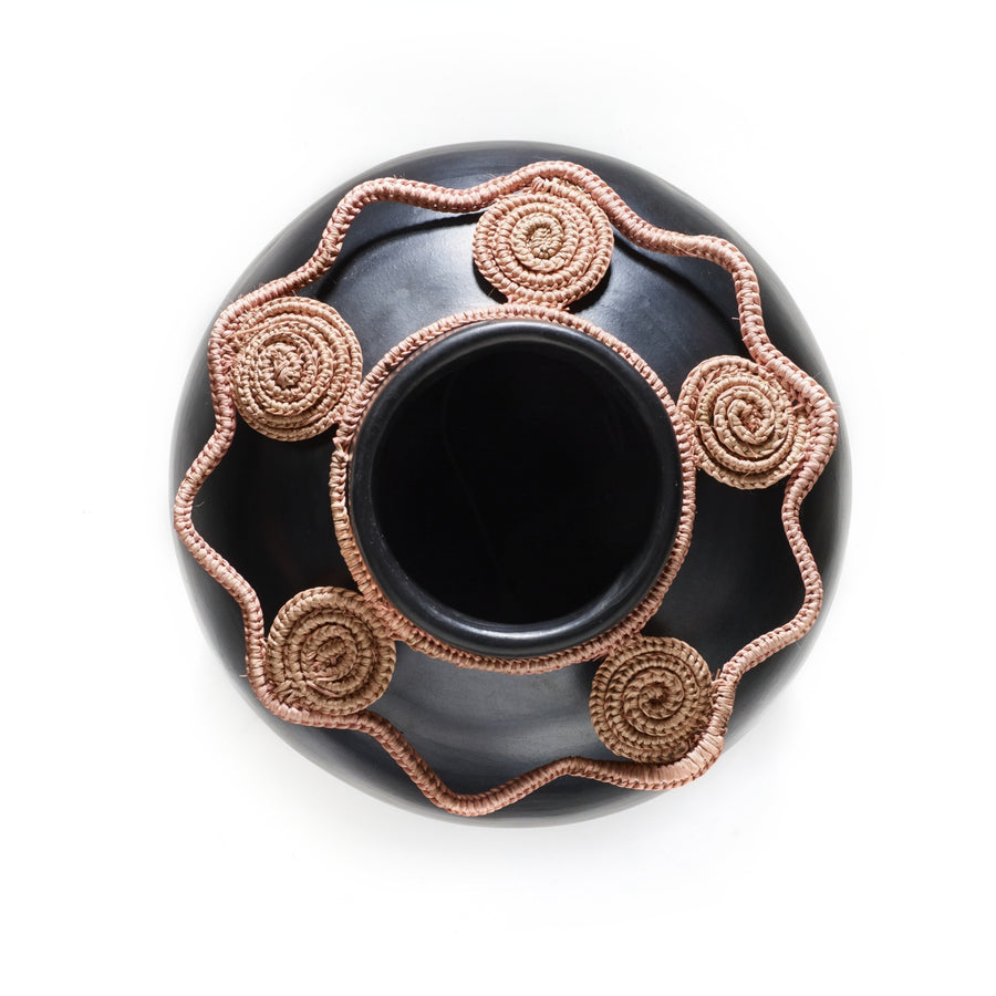 A top view of the Ames Coyar Vase 2 reveals a dark round design featuring intricate beige spirals encircling its smooth surface. The spiral pattern is reminiscent of traditional wickerwork and is connected by a wavy line, creating an ornate look around the vases wide opening.