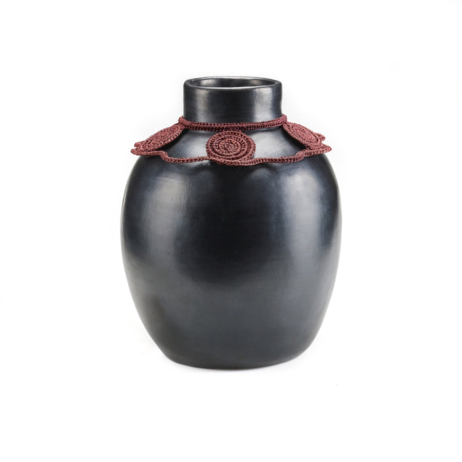 The Coyar Vase 2 by Ames is a sleek black ceramic piece with a smooth finish and a decorative maroon crochet band showcasing circular patterns around the neck, set against a plain white background to highlight its elegance.
