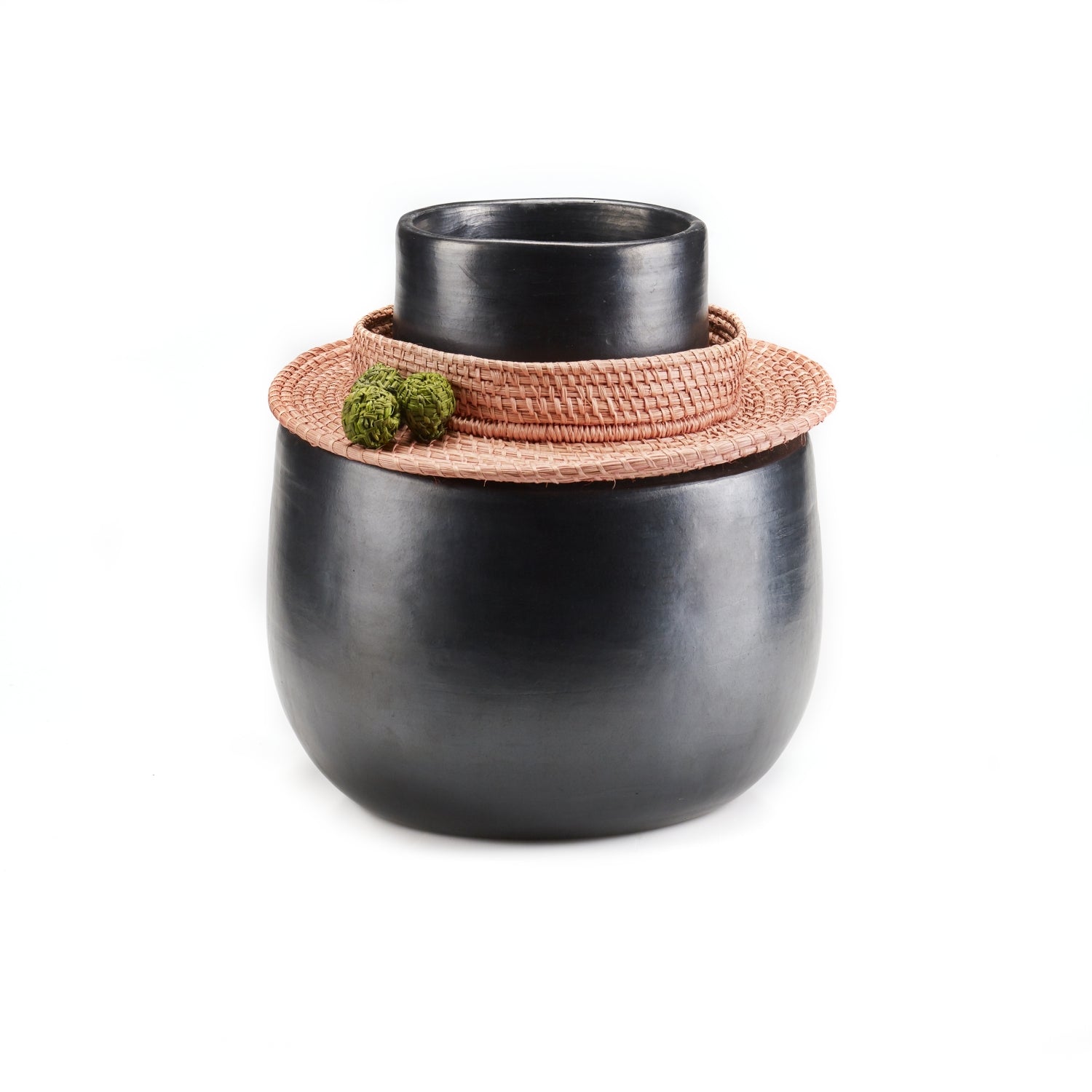 The Coyar Vase 4 by Ames is a matte black ceramic piece with a wide base and narrow top, accented by a Jipi palm wickerwork rattan collar. Two small green moss balls elegantly rest on the collar, adding natural contrast against the plain white backdrop.