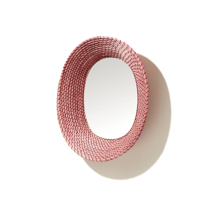 The Ames Killa Mirror by Ames features a handmade woven pink Iraca palm frame in a round design, casting a shadow on a white background.