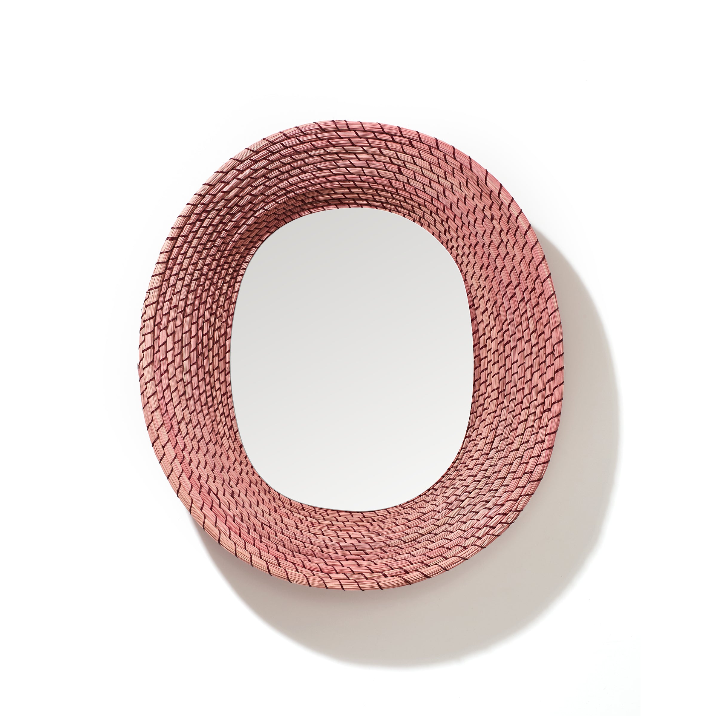 The Ames Killa Mirror by Ames features a round glass center framed by thick, handmade woven pink iraca palm, giving it a textured, basket-like look. Displayed on a white background.