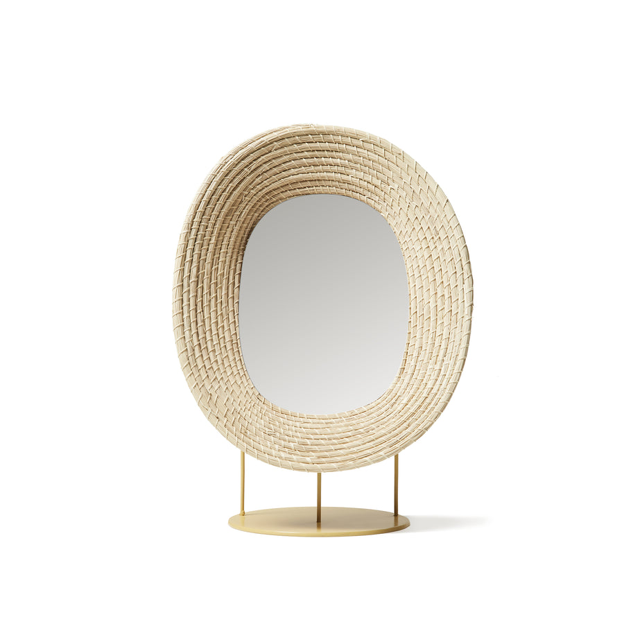 The Ames Killa Standing Mirror by Ames features an oval design with a wide iraca palm rattan frame, set on a round flat gold base with three slim supports, evoking timeless elegance against a plain white background.