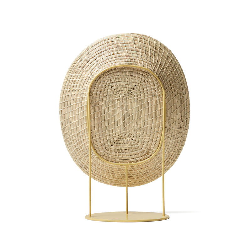 The Ames Killa Standing Mirror by Ames features a large, woven oval frame in light beige, inspired by handmade basket artistry. Supported by a minimalist yellow metal stand and circular base reminiscent of Pauline Deltour’s iconic designs.