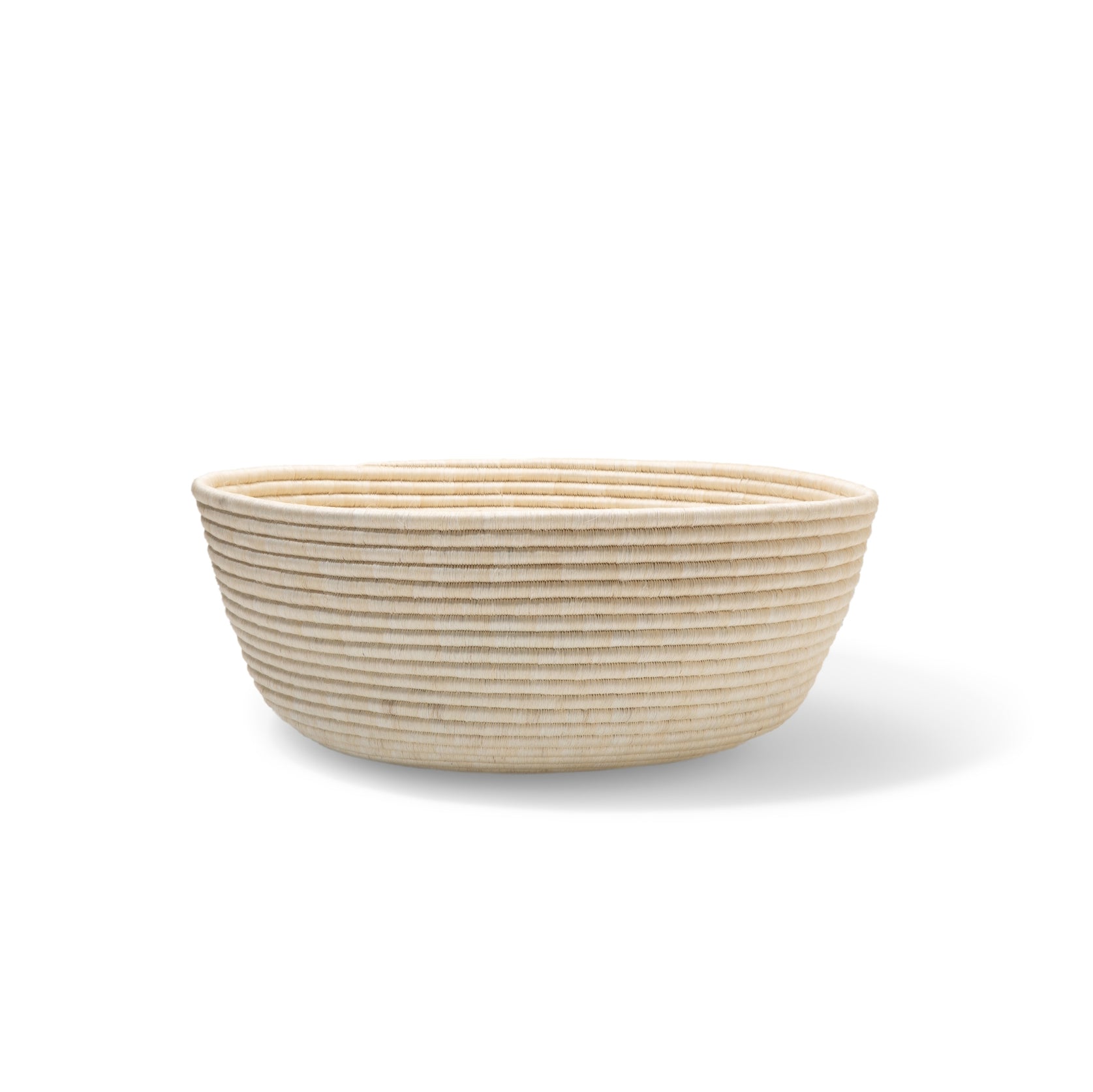 The Ames La Che Basket by Ames is a round, shallow, woven basket with horizontal ridges, handmade from Fique fibers and shown against a plain white background.