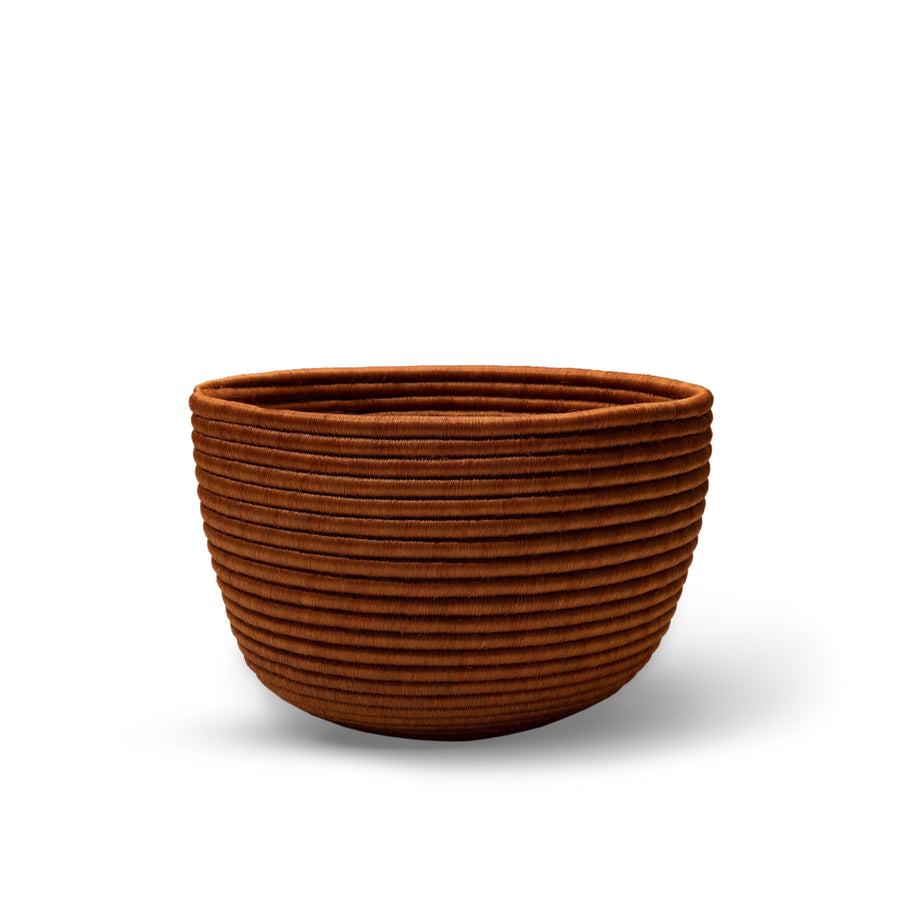 The Ames La Che Basket by Ames features a round, brown design with horizontal ridges, handcrafted from Fique fibers and displayed against a white background.