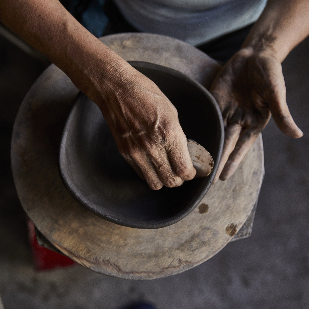 Fingers precisely shape a clay bowl on a pottery wheel, focusing on the hands and wet clay as in the artistry of Colombian crafts, with Ames Loza Ceramics known for exquisite black designs.