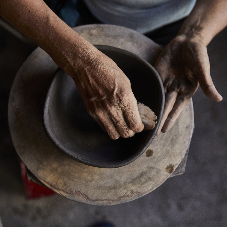 Fingers precisely shape a clay bowl on a pottery wheel, focusing on the hands and wet clay as in the artistry of Colombian crafts, with Ames Loza Ceramics known for exquisite black designs.