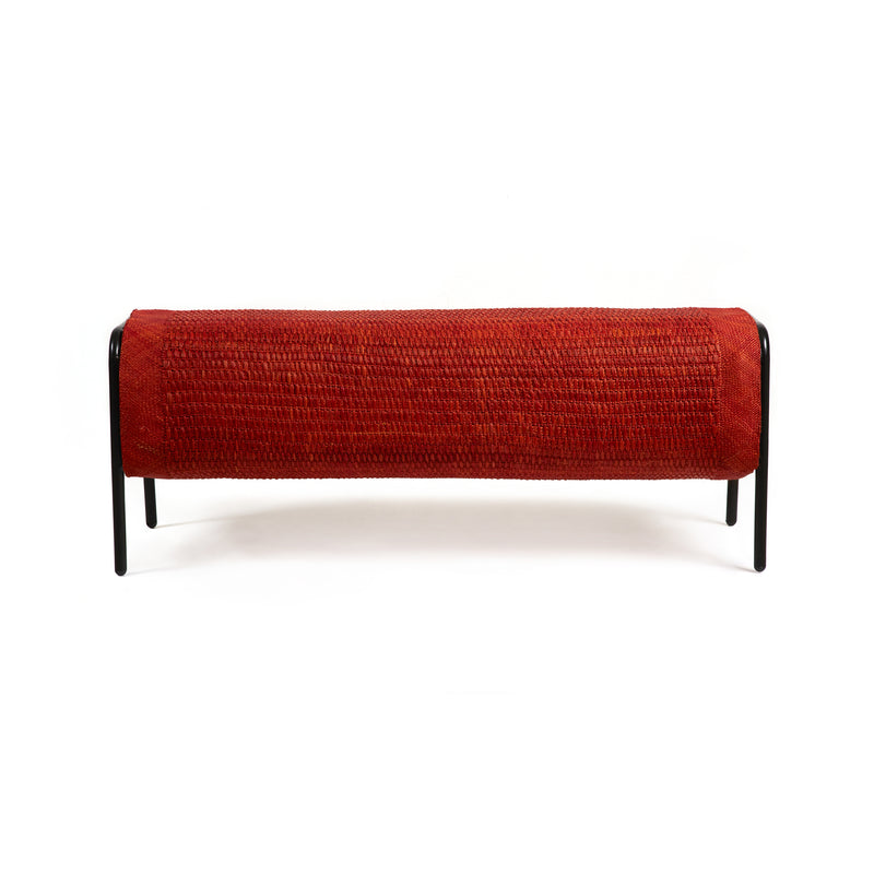 The Ames Mecato Bench by Ames features a cylindrical, textured red cushion on a minimalist black powder-coated steel frame, shown against a white background.