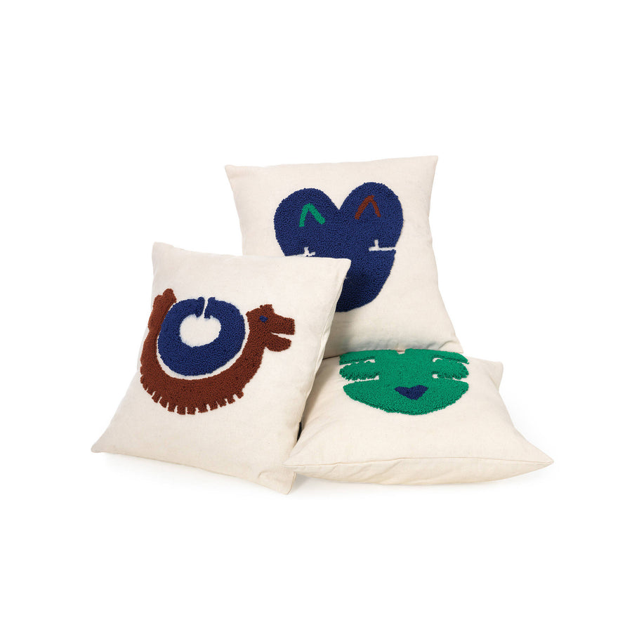 The Ames Nido Pichu cushions by Ames feature whimsical, colorful animal and face designs—a brown and blue snail, a blue heart with green and purple accents, and a green smiling face—showcasing Sebastian Herkner’s joyful, handmade style.