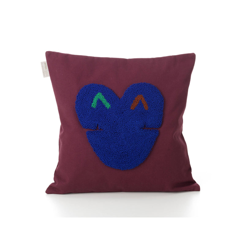 Introducing the Ames Nido Kukuy pillow: a square maroon pillow showcasing a textured blue heart design with abstract green and orange eye-like accents on a plain white 100% cotton background, enhancing its charm.