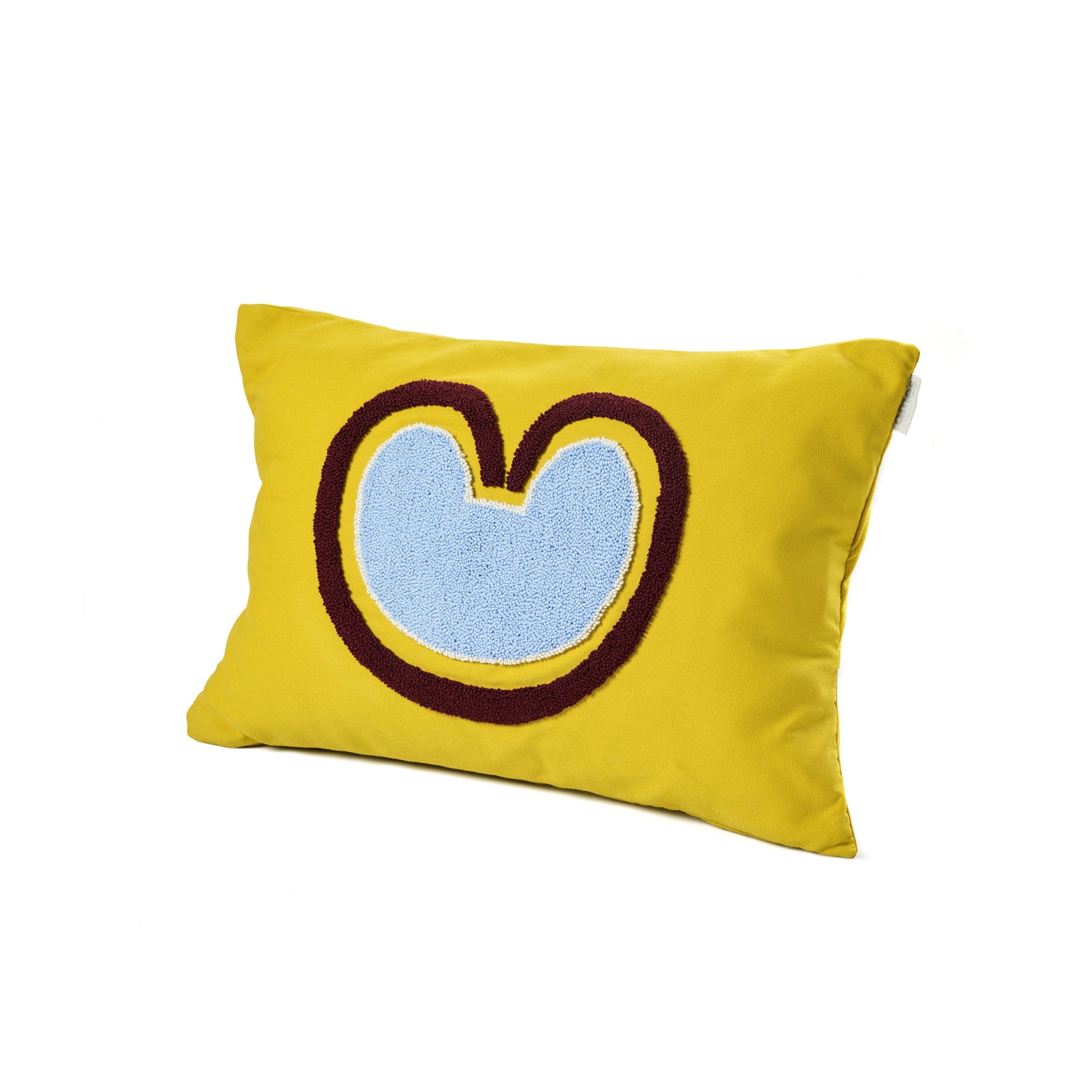 The Ames Nido Coraz cushion by Ames is a rectangular yellow cushion with a large abstract blue shape outlined in brown—resembling a stylized heart or M—perfect for fans of handmade designs and Sebastian Herkner’s creations.