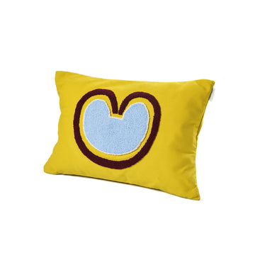 The Ames Nido Coraz cushion by Ames is a rectangular yellow cushion with a large abstract blue shape outlined in brown—resembling a stylized heart or M—perfect for fans of handmade designs and Sebastian Herkner’s creations.