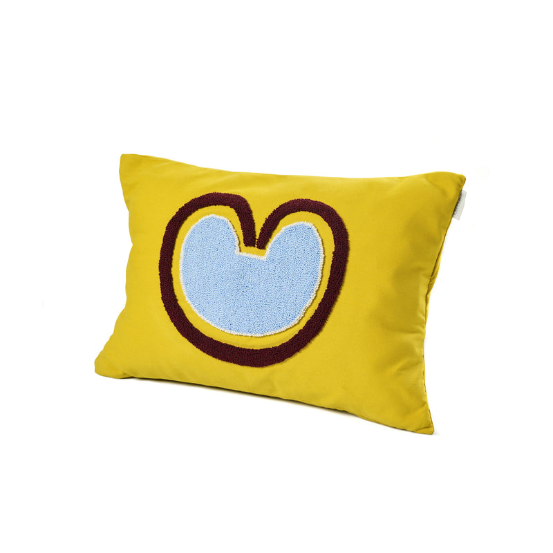 The Ames Nido Coraz cushion by Ames is a rectangular yellow cushion with a large abstract blue shape outlined in brown—resembling a stylized heart or M—perfect for fans of handmade designs and Sebastian Herkner’s creations.
