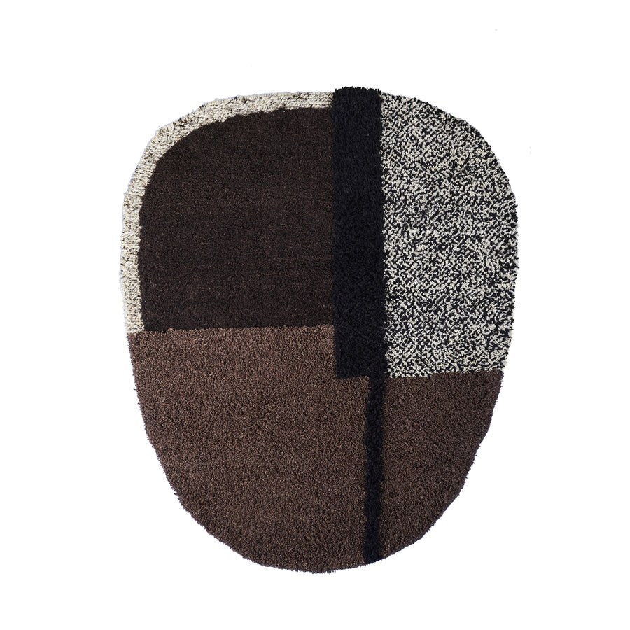 The Ames Nudo Rug showcases Colombian arts and crafts with its abstract, oval shape and textured design. Large blocks of dark brown and speckled gray are separated by a black stripe, forming a slightly asymmetrical pattern for a modern, artistic look.