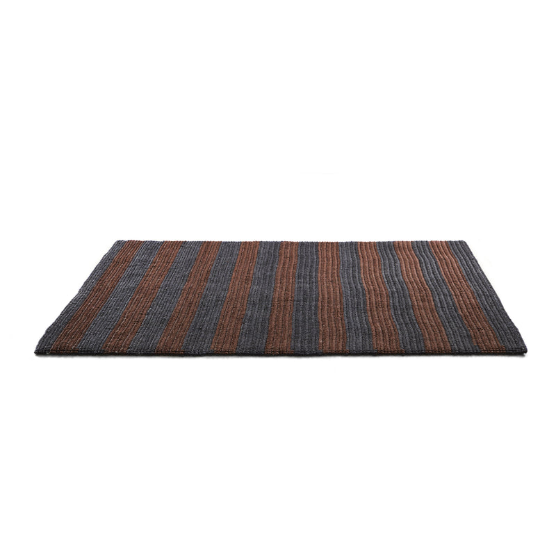 The Ames Par Raya Rug features a rectangular design with alternating dark gray and brown vertical stripes, crafted from natural fibers for an elegant woven texture against a plain white background.