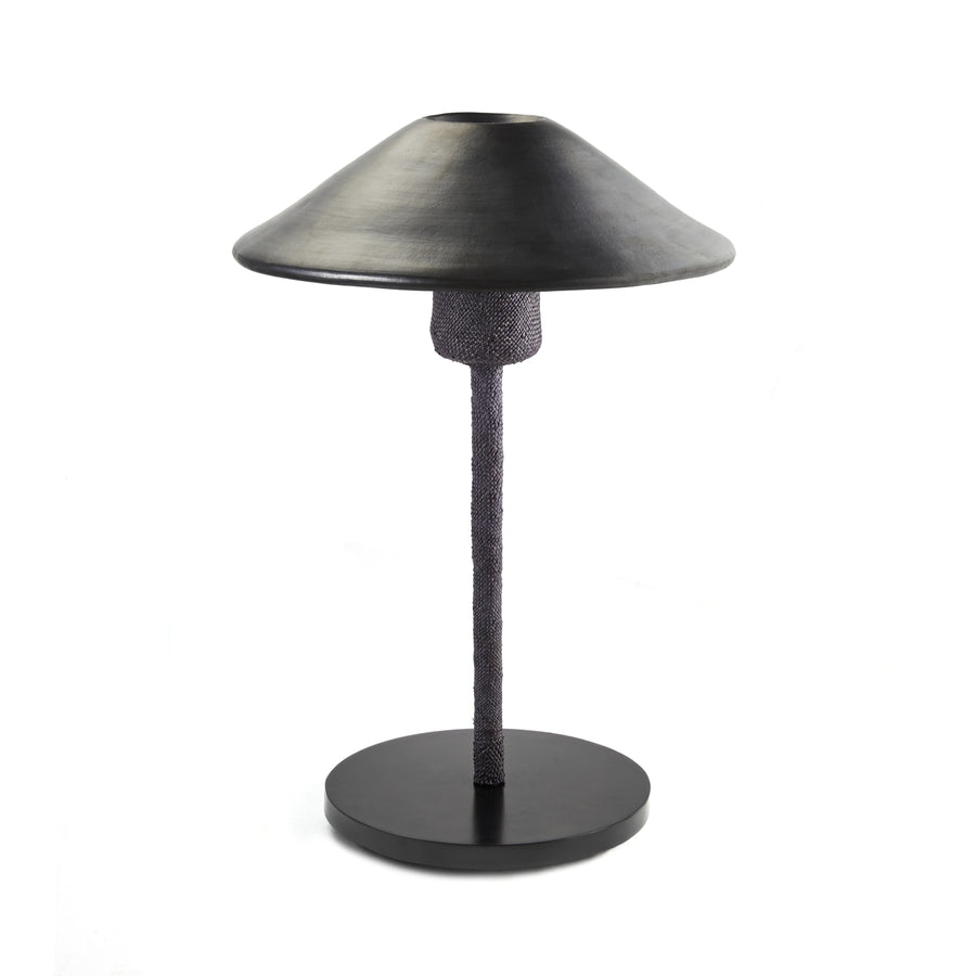 The Raiz Table Lamp by Ames features a sleek black design with a Colombian-inspired ceramic shade, wide cone-shaped metal structure, and textured cylindrical stem, all supported by a round base set against a plain white background.