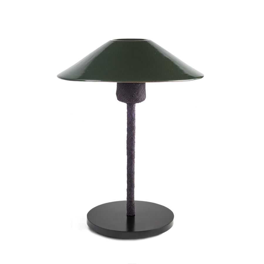 The Raiz Table Lamp by Ames features a dark green, wide conical ceramic shade that reflects Colombian craftsmanship. It has a textured, dark stand and a round, flat base, showcased against a plain white background.