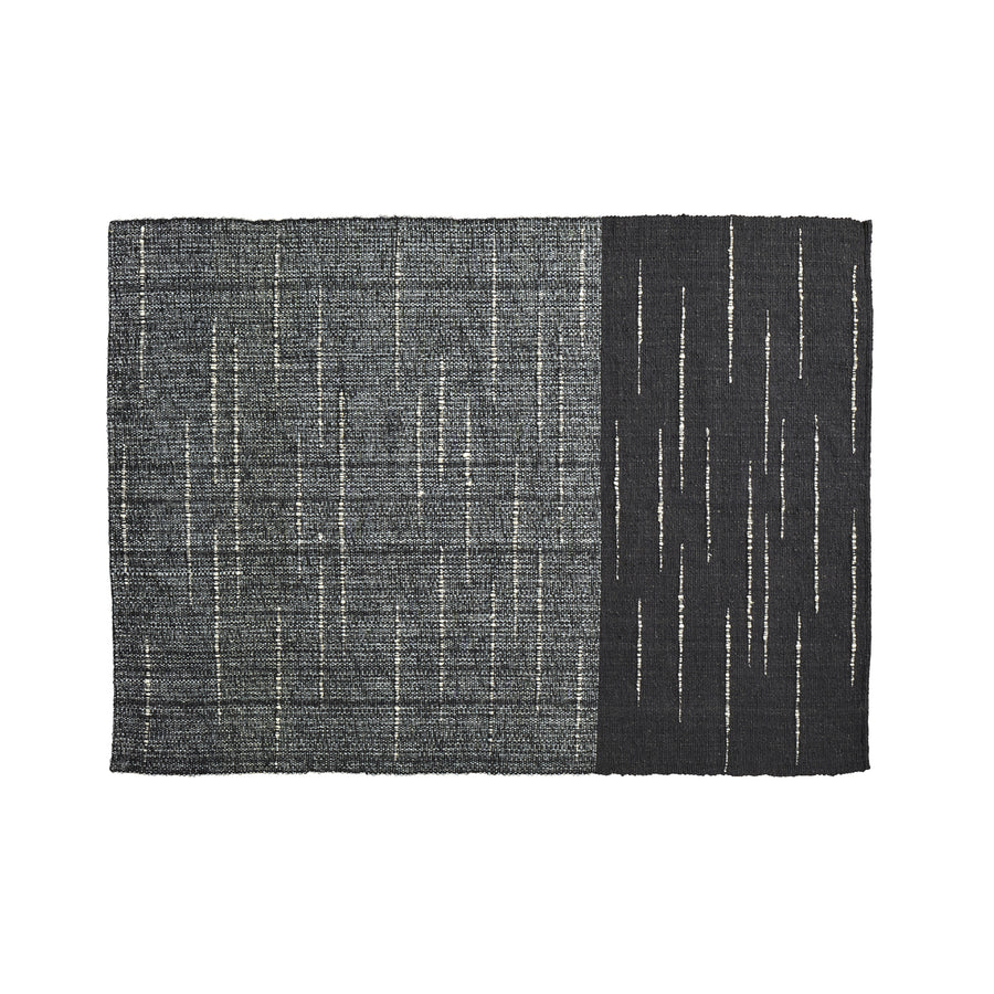 The Ames Subas Rug by Ames is a rectangular wool rug with a dark, speckled gray left side and solid black right side, both accented by thin, irregular vertical white lines in a scattered pattern.