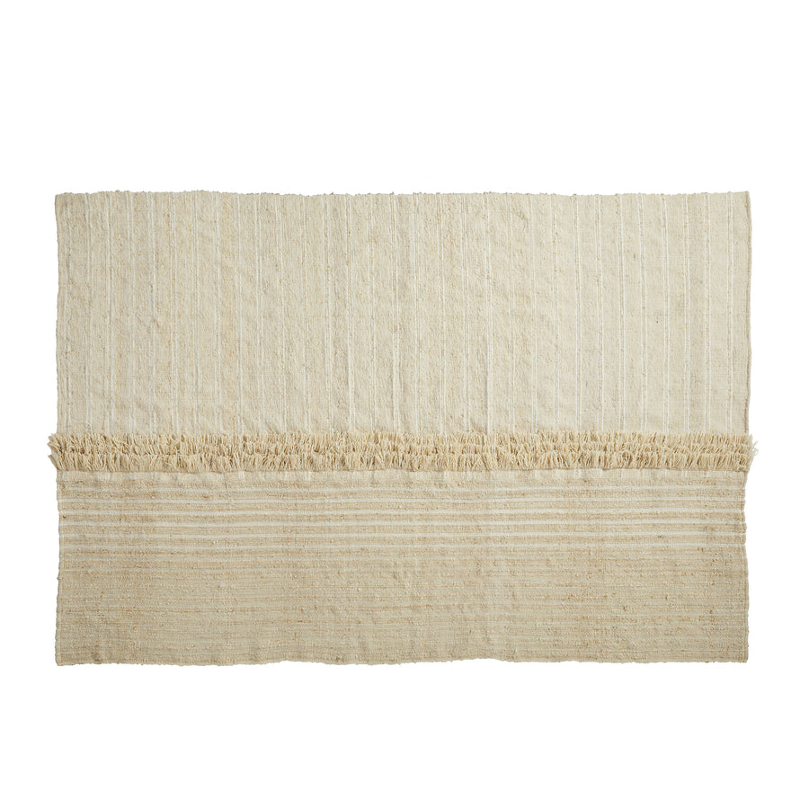 The Ames Subas Rug by Ames is a rectangular cream-colored wool rug featuring subtle horizontal stripes and a fringed band near one end, displayed on a white background and designed by Sebastian Herkner.