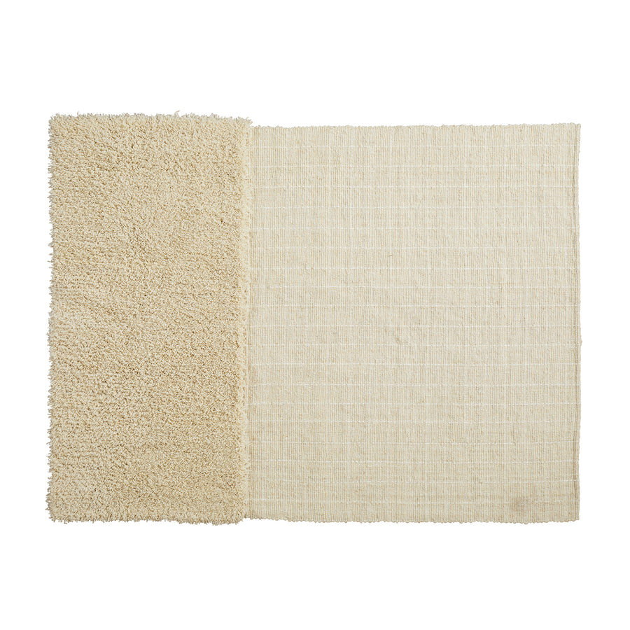 The Ames Subas Rug by Ames is a rectangular beige wool rug with two textures: the left side is shaggy and fluffy, while the right side is flat and woven, offering a striking visual contrast.