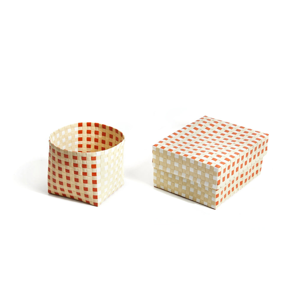 The Suncho Baskets collection by Ames includes a hand-made woven cylindrical basket and rectangular box with lids, both in a red and cream checkered pattern. Made from recycled Polypropylene, these items rest elegantly against a plain white backdrop.