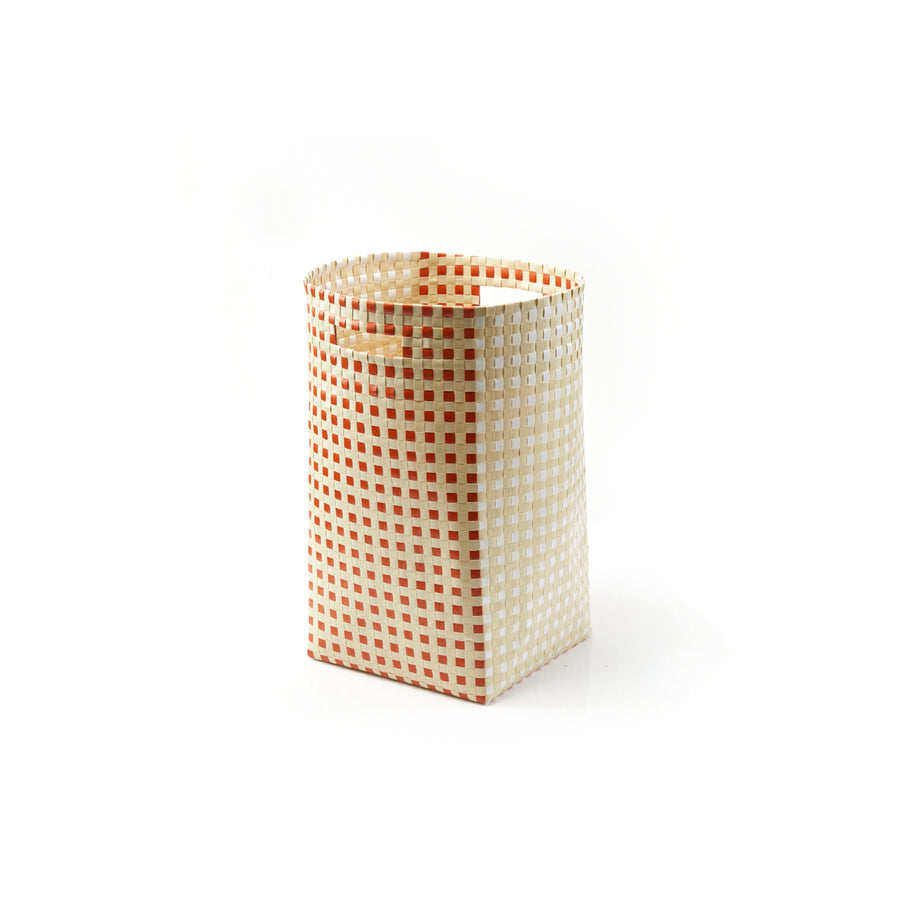 The Suncho Basket by Ames, crafted from recycled polypropylene, is a tall cylindrical piece with red and white checkered patterns. This hand-made storage item features an open top and reflects Pauline Deltours signature style, all set against a plain white background.