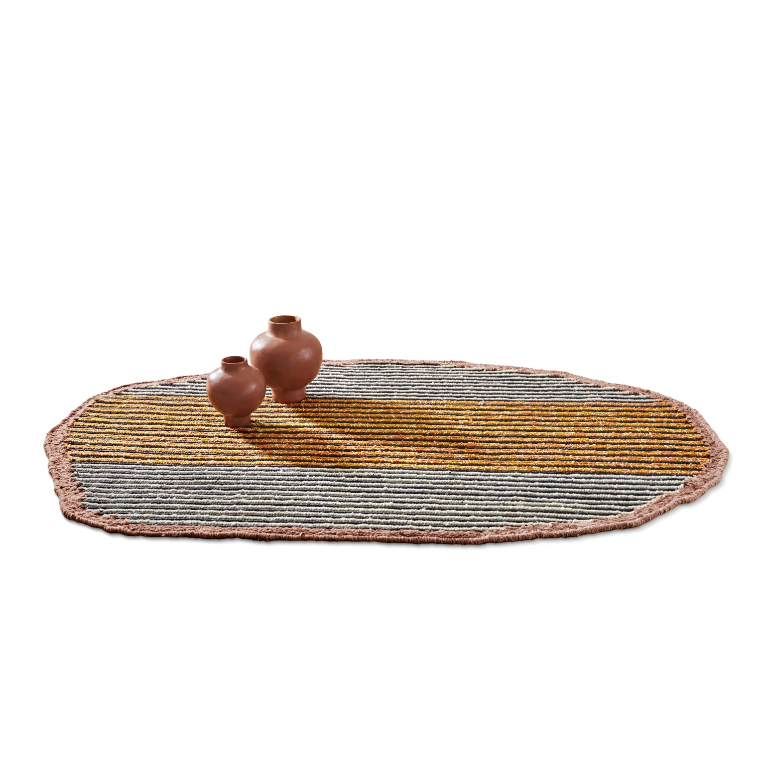 The Uilas Noche Rug by Ames is an oval-shaped rug with multicolored stripes in grey, yellow, and pink tones. It features a textured border crafted from black dyed fique fiber. Two brown earthen vases on the rug add luxury against the plain white background.
