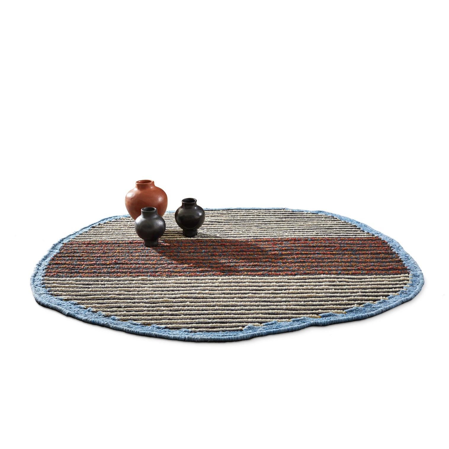 The Ames Uilas Noche Rug, round and textured with a blue border and striped in beige, brown, and red hues, features three earthy pottery jars crafted from black dyed fique fiber for a luxurious effect—two black and one terracotta resting on the rug against a white backdrop.