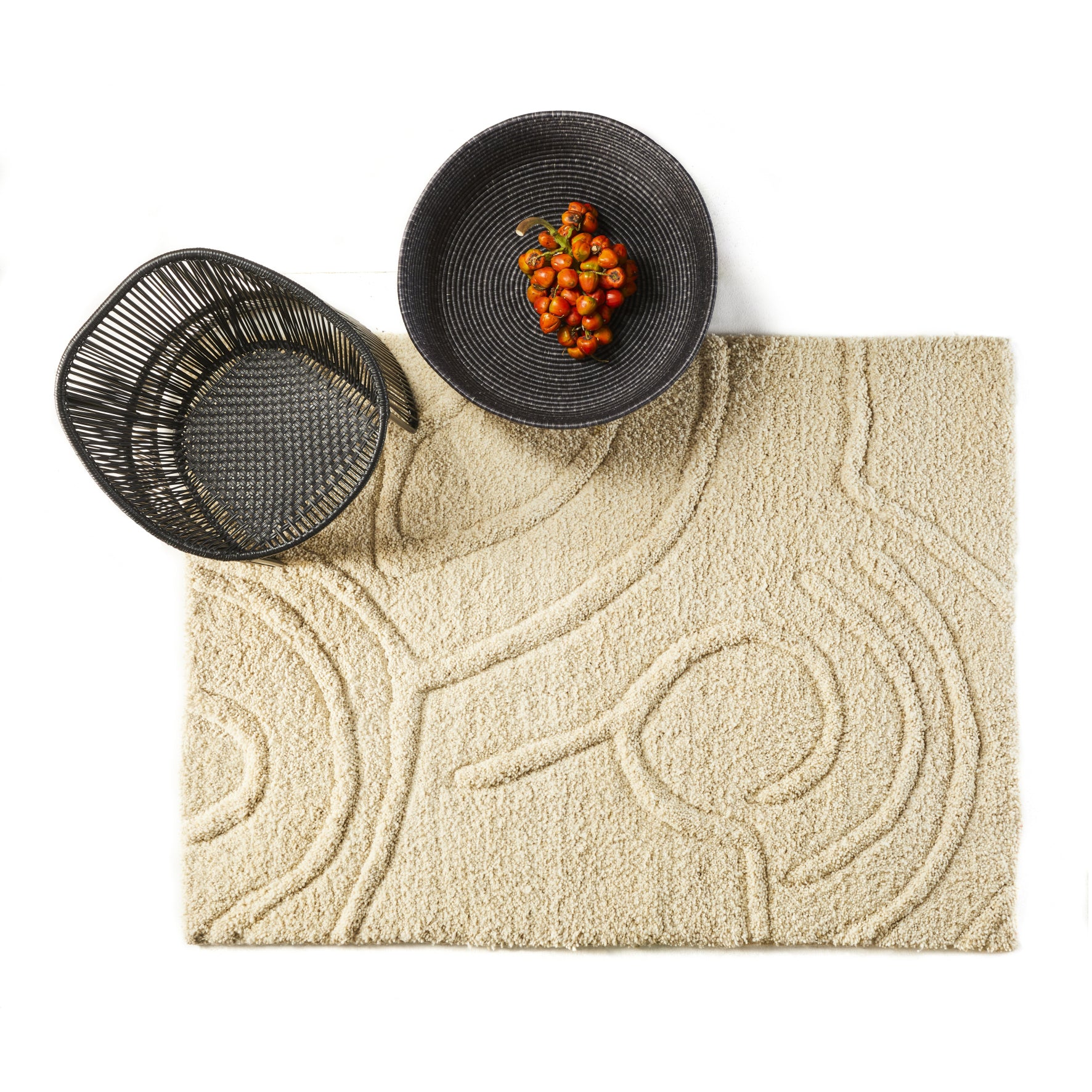 A woven chair and a bowl with cherry tomatoes rest on Ames’ Zenues Rug, showcasing the swirling patterns inspired by Zenu culture.