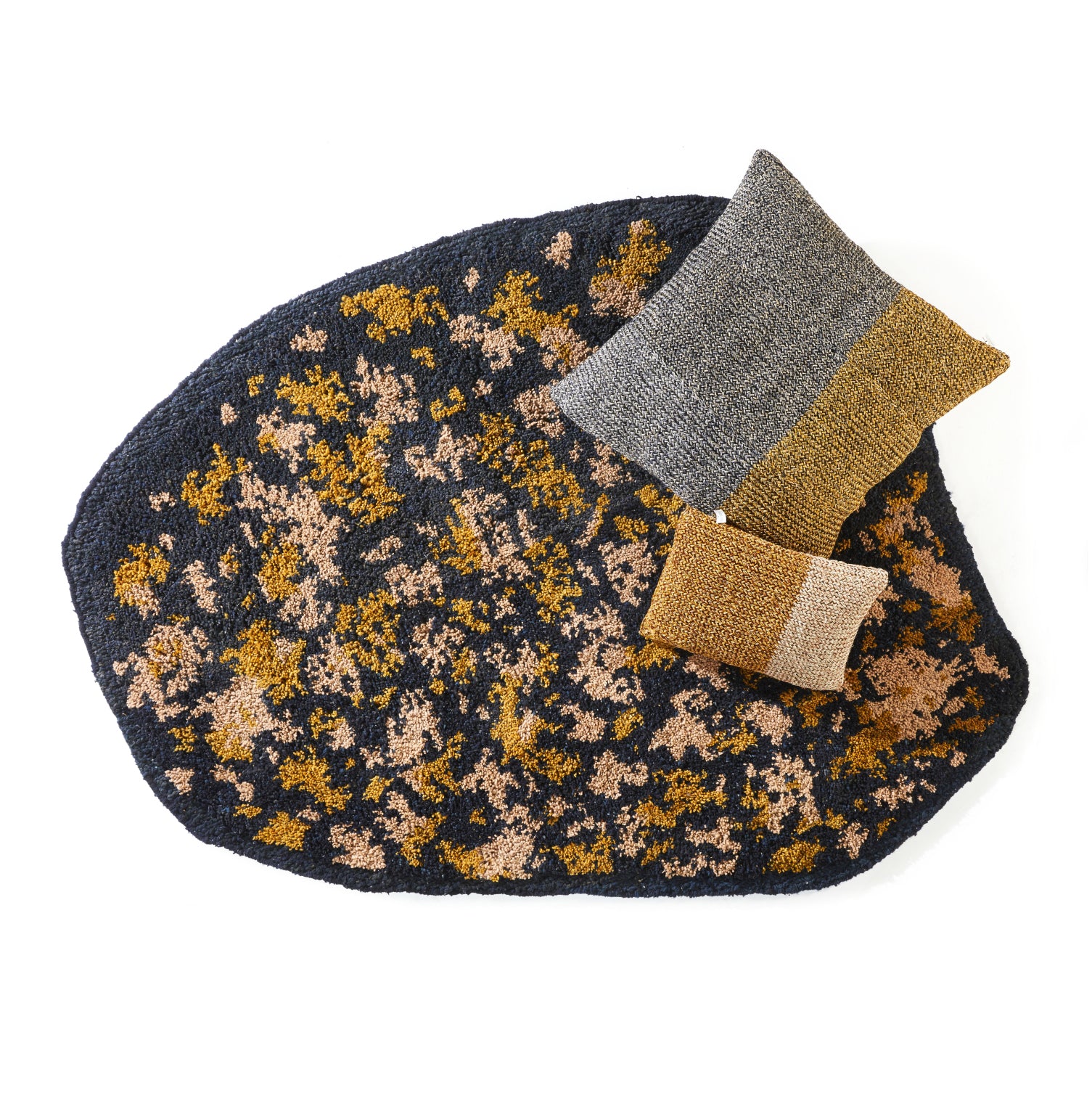 The Ames Zipa Rug by Ames features an abstract, irregular design in dark tones with gold, tan, and beige speckles, complemented by two textured rectangular pillows in gray, gold, and copper.