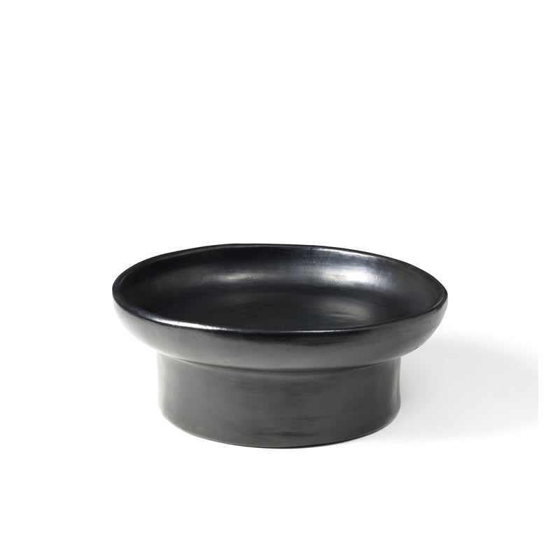 The Barro Tray 1 by Ames features a sleek, black ceramic design with a wide, shallow basin and thick cylindrical base, showcasing the artistry of Colombian manufacturing against a plain white background.