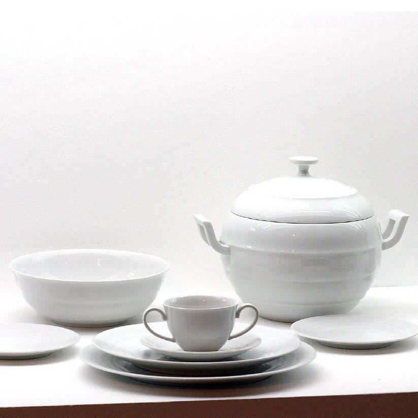 The Augarten Opus Collection is showcased elegantly on a pristine surface, featuring a white ceramic lidded soup tureen, bowl, teacup with saucer, and dinner plates, all echoing the timeless artistry of Vienna Porcelain.