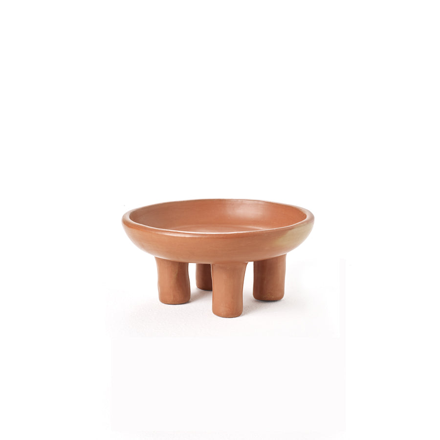 The Ames Barro Tray 1 by Ames is a round, shallow terracotta bowl with four short legs, set against a white background, highlighting the craftsmanship of handmade Colombian ceramics and traditional pottery.