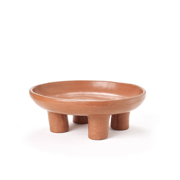 The Ames Barro Tray 1 by Ames is a round, shallow brown clay bowl with four short cylindrical legs, photographed on a white background, highlighting the craftsmanship of handmade Colombian ceramics.