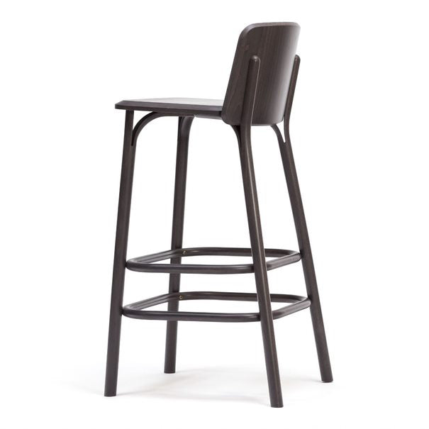 The Barstool Split from TON is a tall, dark brown wooden piece featuring a curved backrest and two horizontal footrests. Its sleek design reflects modern sophistication with a smooth finish that showcases its minimalist appeal, reminiscent of Arik Levys aesthetic mastery.