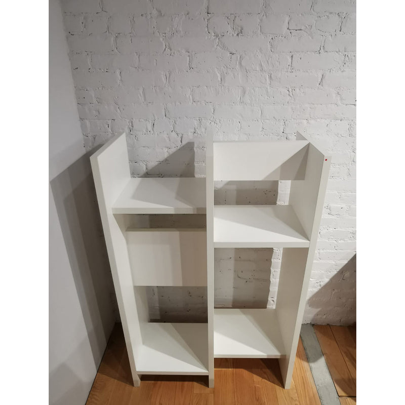 The E15 SH05 ARIE shelf, standing against a textured white brick wall on a light wood floor, features a unique cubic pattern with varied open compartments, serving as an elegant shelving wall that enhances the rooms modern aesthetic.