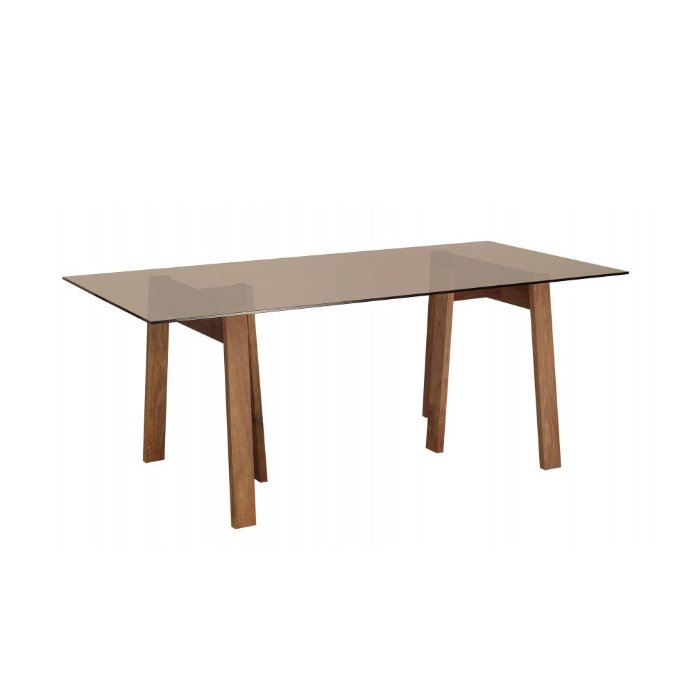 The DC08 Basis Trestle by E15 is a rectangular glass-top table featuring four outward-angled wooden legs crafted from solid wood trestles. Its clear glass surface highlights the sturdy BASIS table tops and minimalist wooden base beneath.