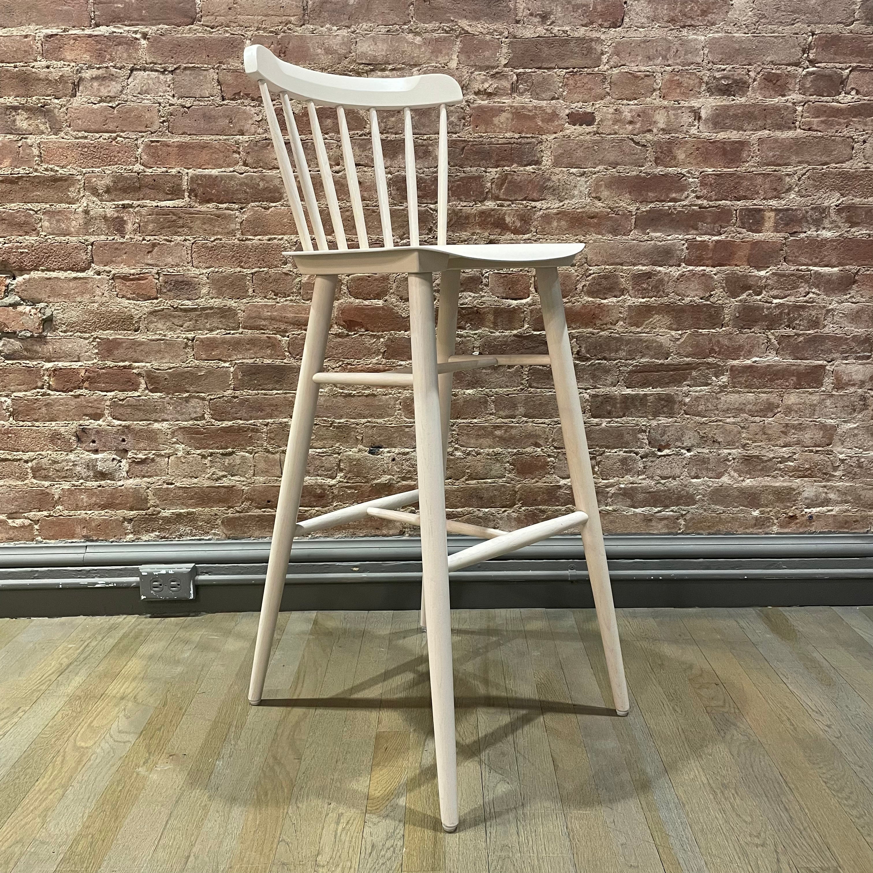 A tall, light oak Barstool Ironica by TON with a backrest and footrest stands on a wooden floor against a rustic brick wall.