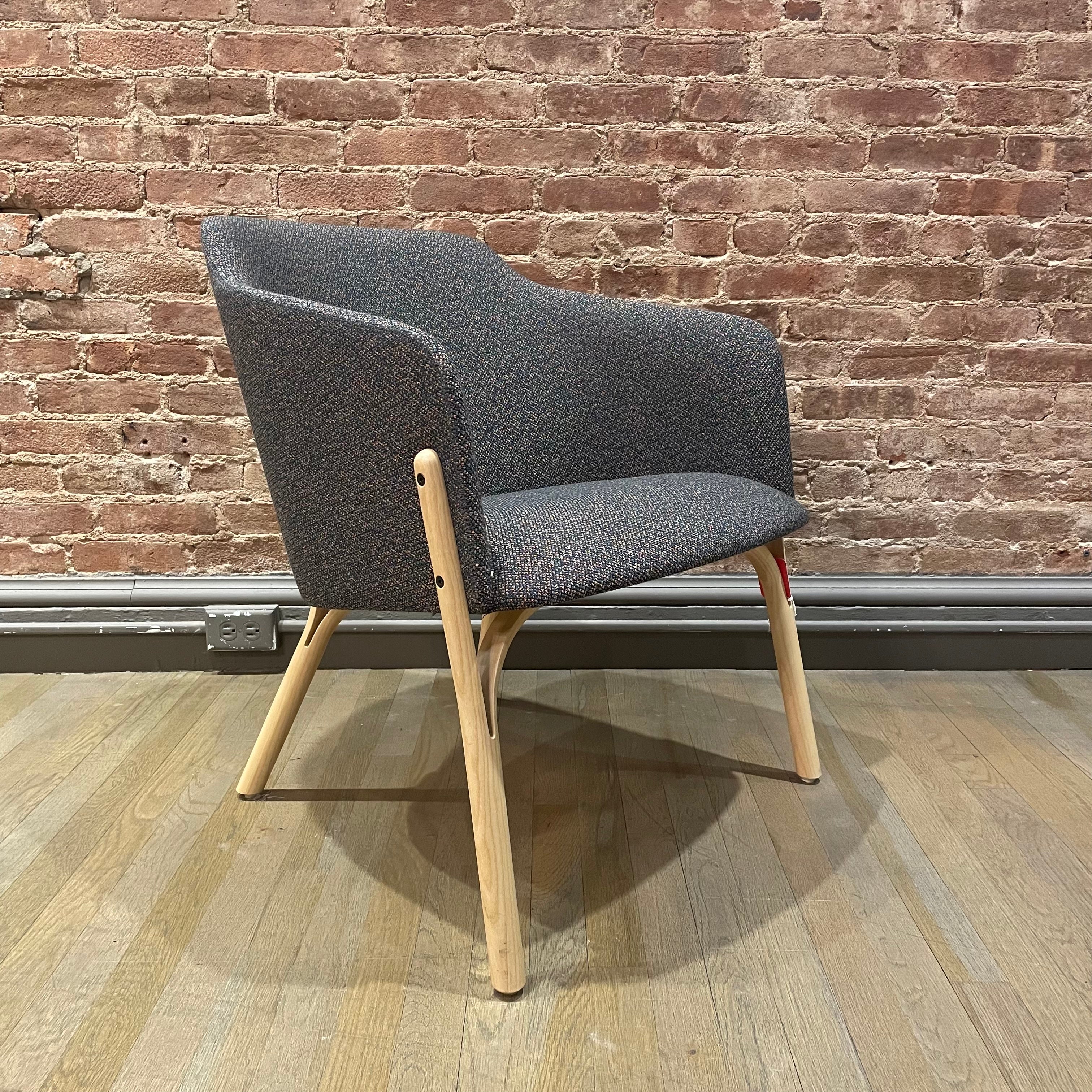 The Lounge Chair Split by TON features ergonomic gray fabric seating and wooden legs. Its placed on a hardwood floor against an exposed brick wall, featuring a manually crafted curved backrest with clean lines for a minimalist style.