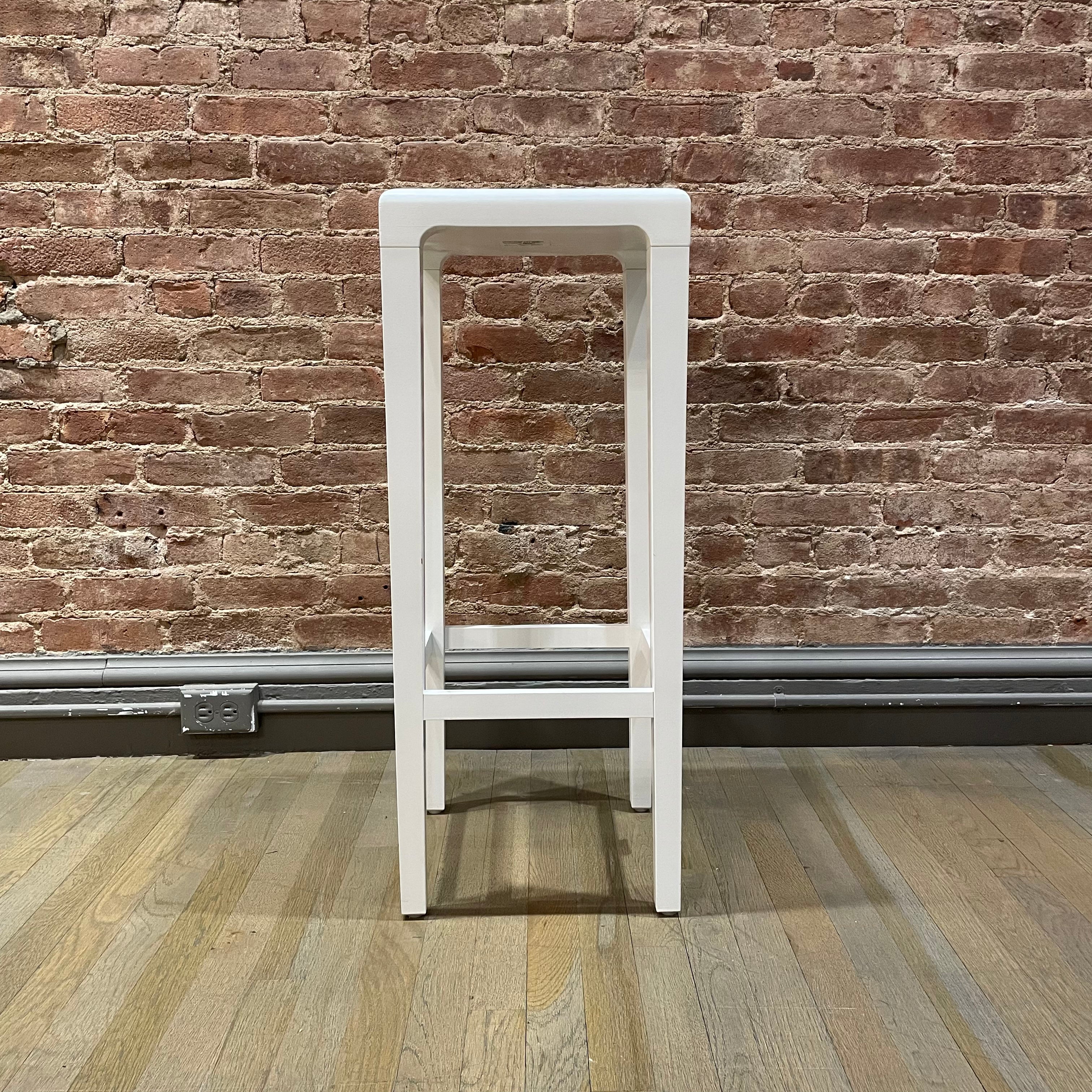 A tall, white Barstool Rioja by TON with a minimalist design stands on a wooden floor against a rustic brick wall, ready for NYC pickup.