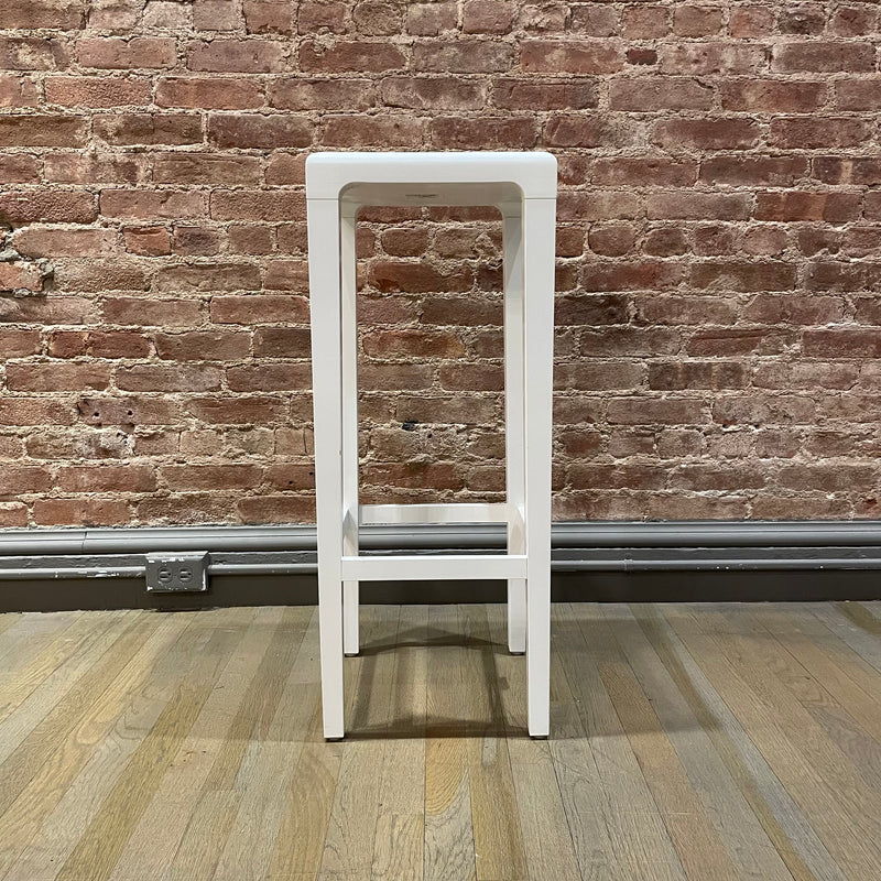 A tall, white Barstool Rioja by TON with a minimalist design stands on a wooden floor against a rustic brick wall, ready for NYC pickup.