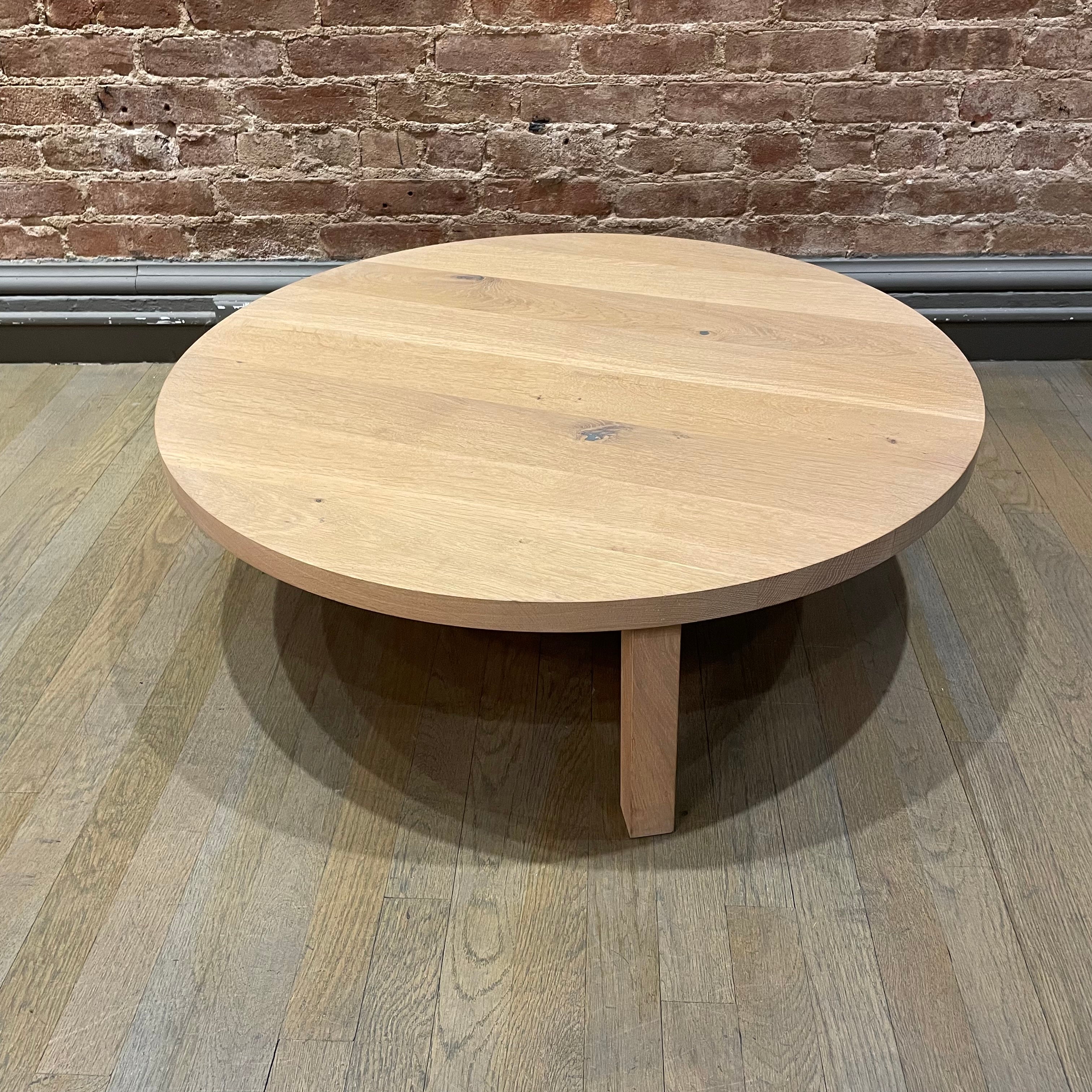 The PA05 LEILA by E15, a minimalist coffee table in solid European oak on wooden floors, boasts a light surface and three angled legs, enhanced by a brick wall backdrop.