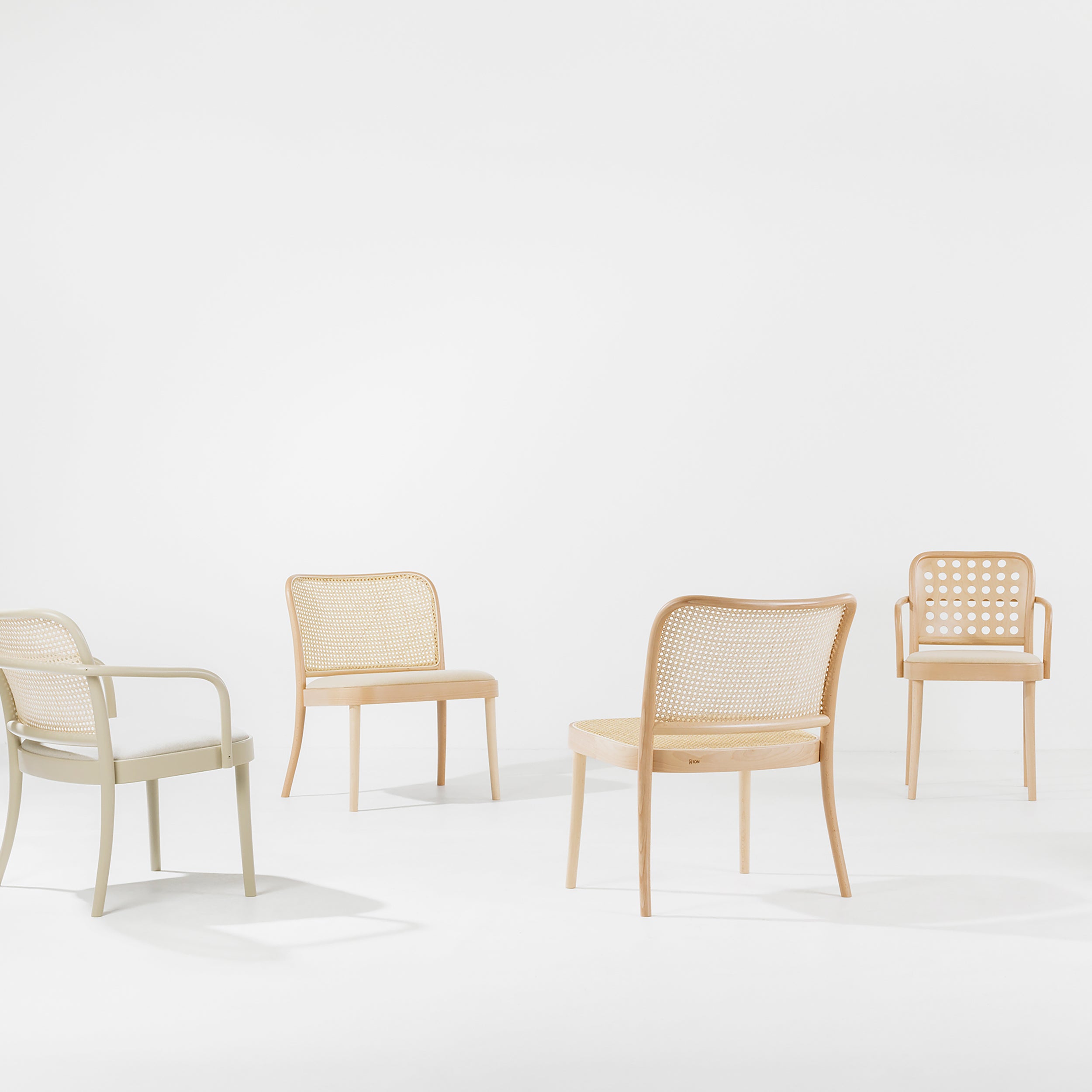Four TON Loungechair 811 wooden chairs with woven cane backs, inspired by Claesson Koivisto Rune, form a circle on a white background. Each chair features distinct armrests and patterns, creating an inviting ambiance with gentle shadows.