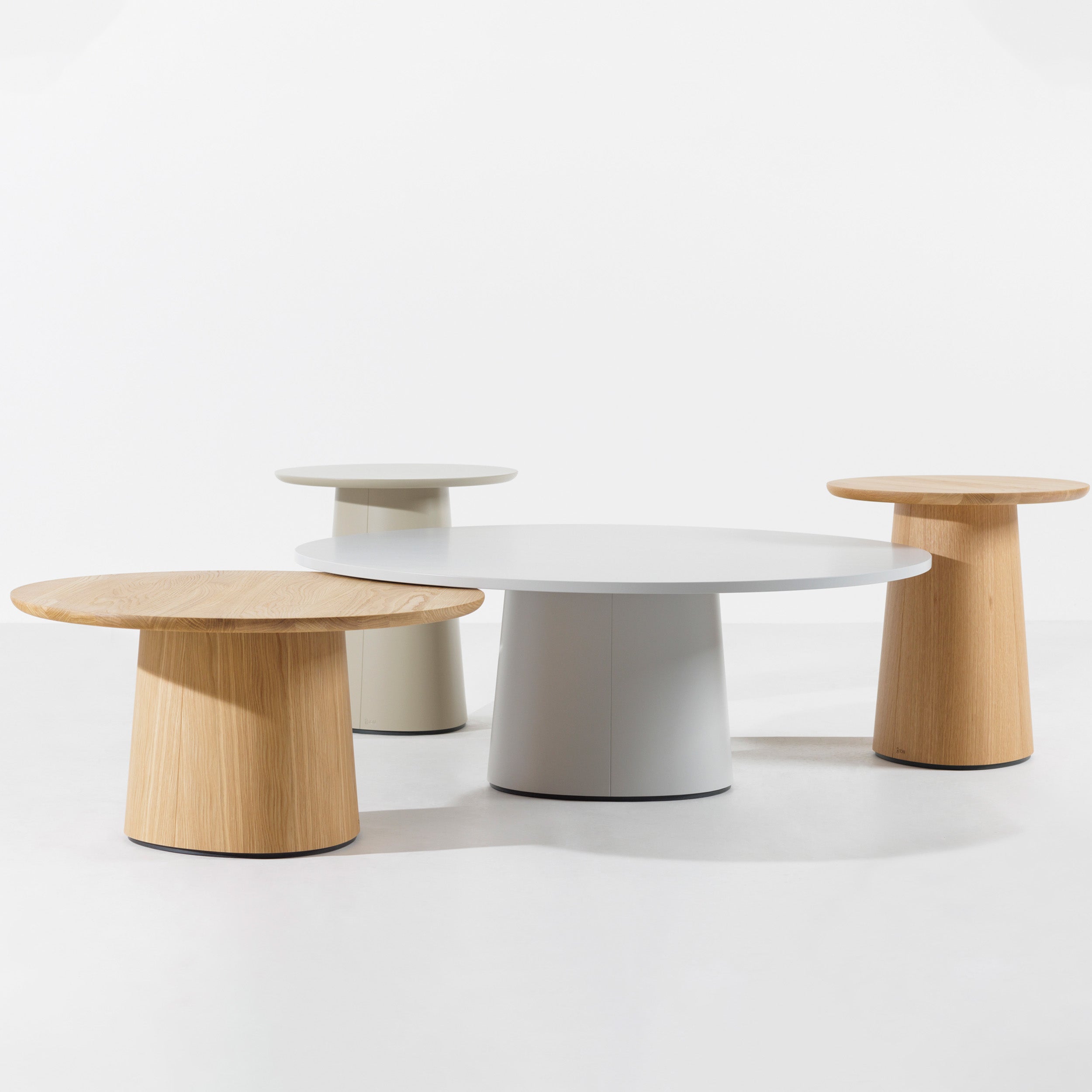 The P.O.V. Coffee Table 474/475 set by TON includes three modern, cylindrical tables with flat, round tops. Two sport a light solid wood finish and one is elegantly white. Varying in height, the tallest stands in the center against a plain white backdrop, creating a coffee table aesthetic.