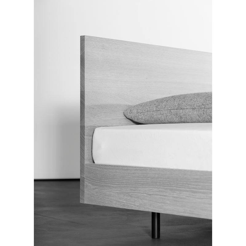 The Iku Bed Series by Sanktjohanser features a solid wood minimalist frame with a light finish and simple headboard, complemented by a white mattress and gray pillow. The room exudes modern elegance with its sleek design, dark flooring, and soft neutral palette.